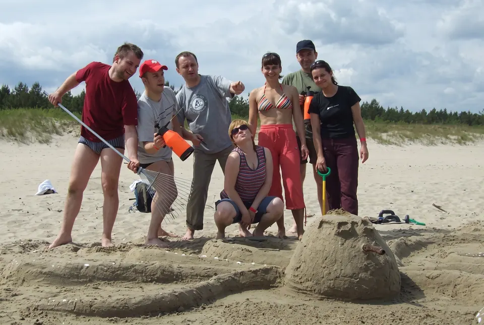 Uczestnicy z łopatkami pozują przy rzeźbie z piasku na plaży