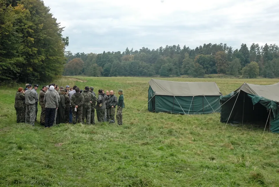 Grupa w mundurach moro na łące obok wojskowych namiotów