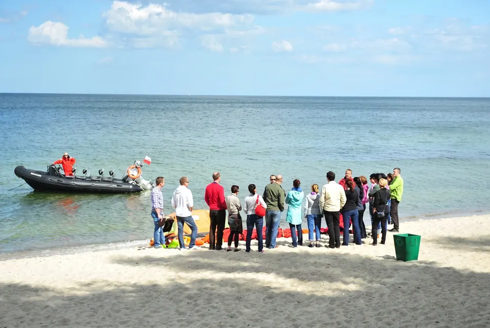 Grupa na plaży obserwuje ponton ratowniczy płynący przy brzegu