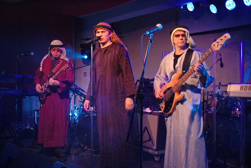 Muzycy w arabskich strojach grają na scenie w niebieskim świetle