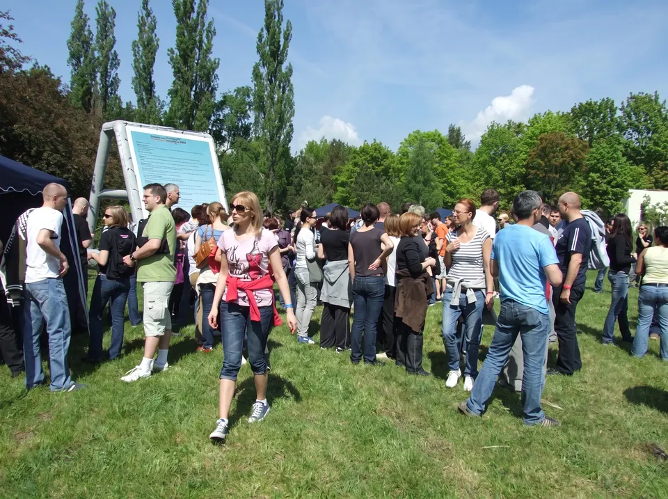 Tłum uczestników na łące przy dużej tablicy z zasadami gry