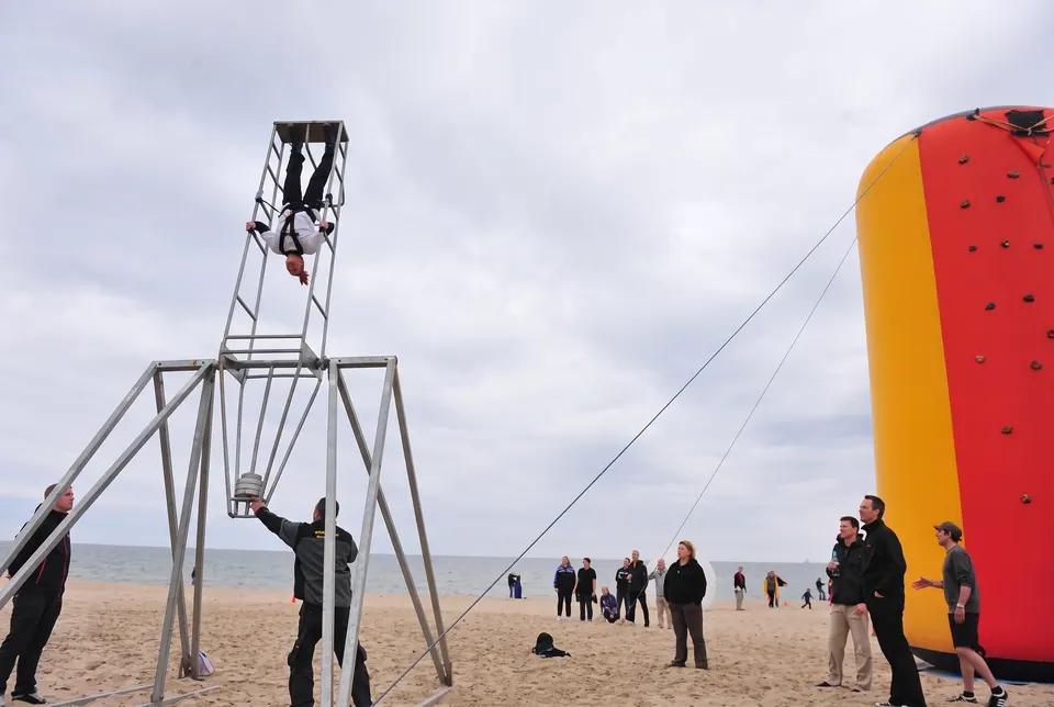 Uczestnik zwisa głową w dół na szczycie metalowej wieży na plaży