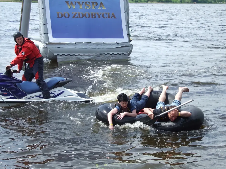 Dwoje uczestników płynie na dętce obok ratownika na skuterze wodnym