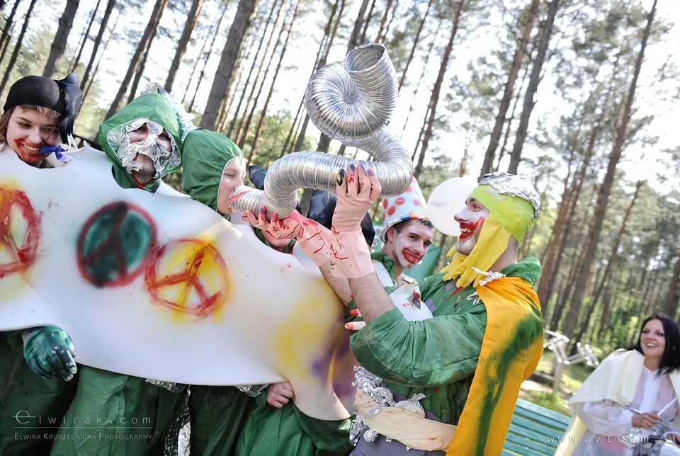 Przebrani uczestnicy z zielonymi twarzami niosą transparent z symbolami pokoju