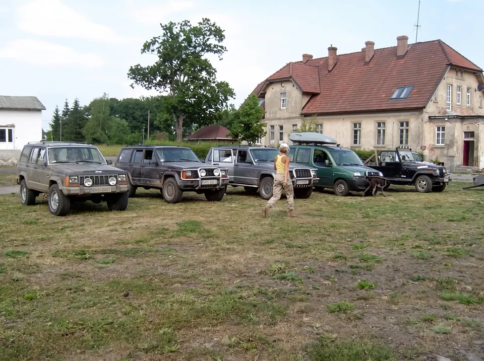 Samochody terenowe zaparkowane na łące przed budynkiem z czerwonym dachem