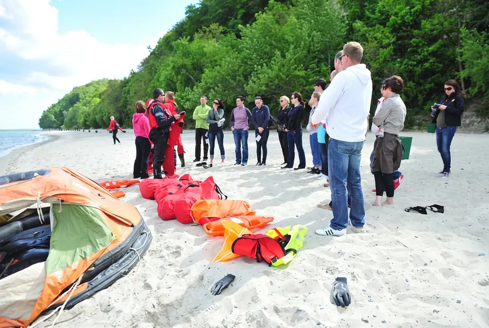 Grupa na plaży przy rozłożonej tratwie ratunkowej i kamizelkach
