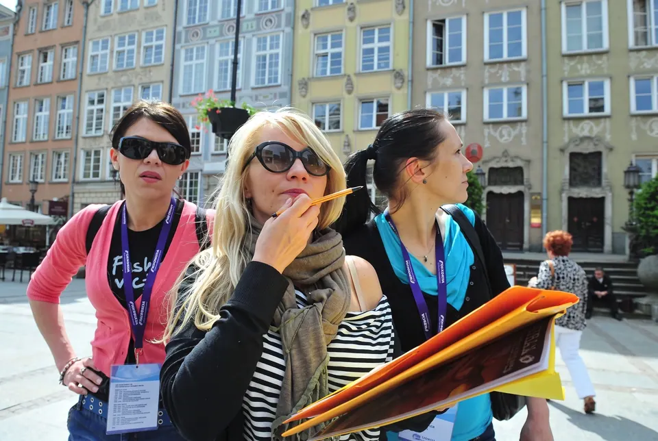 Uczestniczki gry miejskiej z identyfikatorami i teczką zadań przy kamienicach