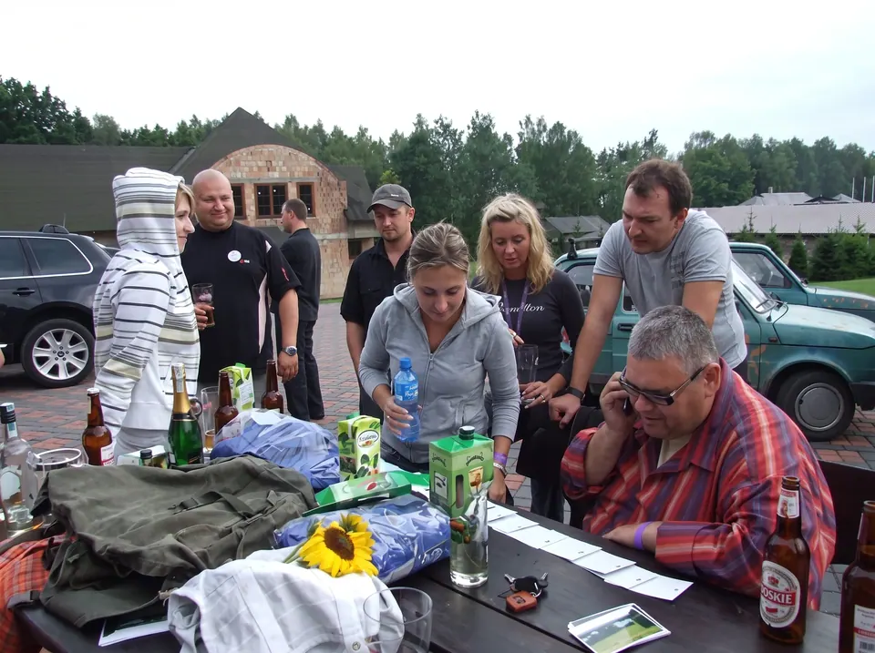 Uczestnicy przy stole z napojami i kartami zadań przed budynkiem