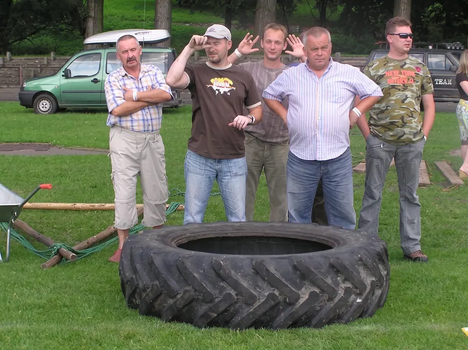Uczestnicy stoją za dużą oponą od ciągnika na trawniku