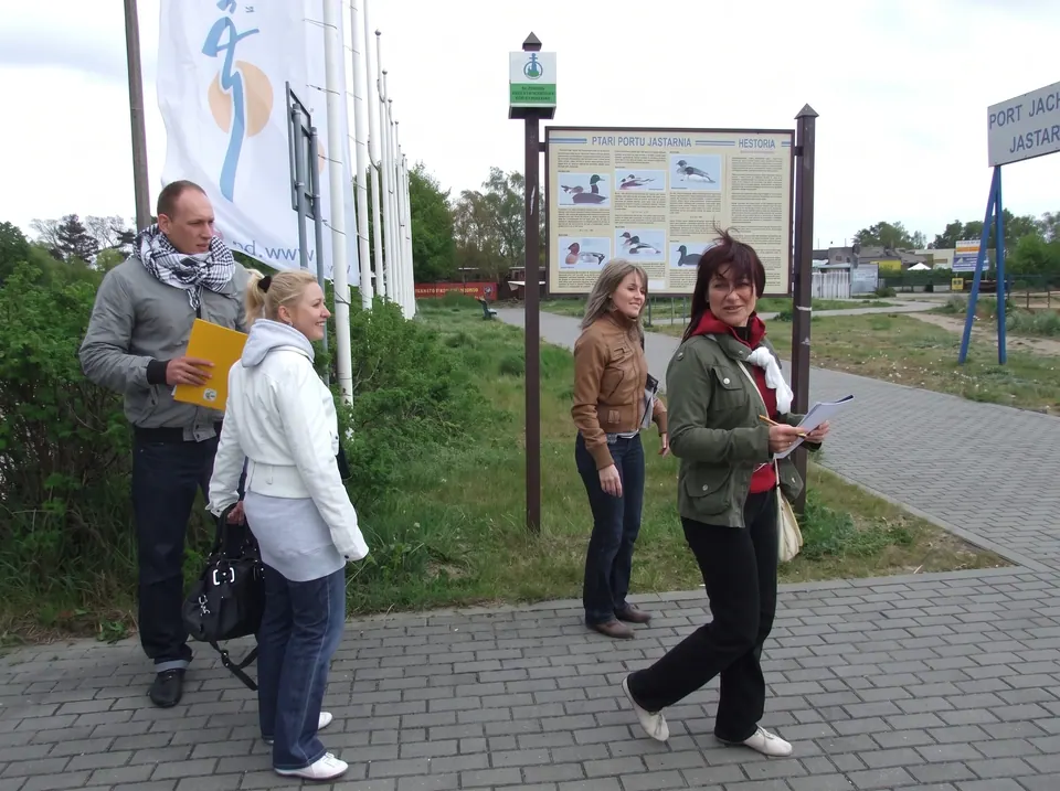 Uczestnicy gry terenowej z kartami zadań przy tablicy informacyjnej