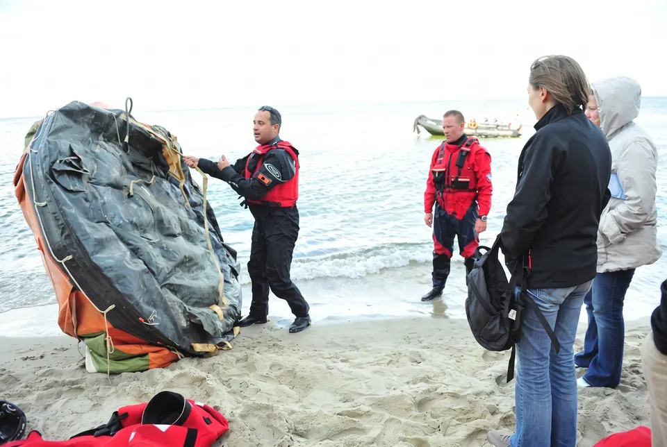 Ratownicy w suchych skafandrach przy rozkładanej tratwie ratunkowej na plaży