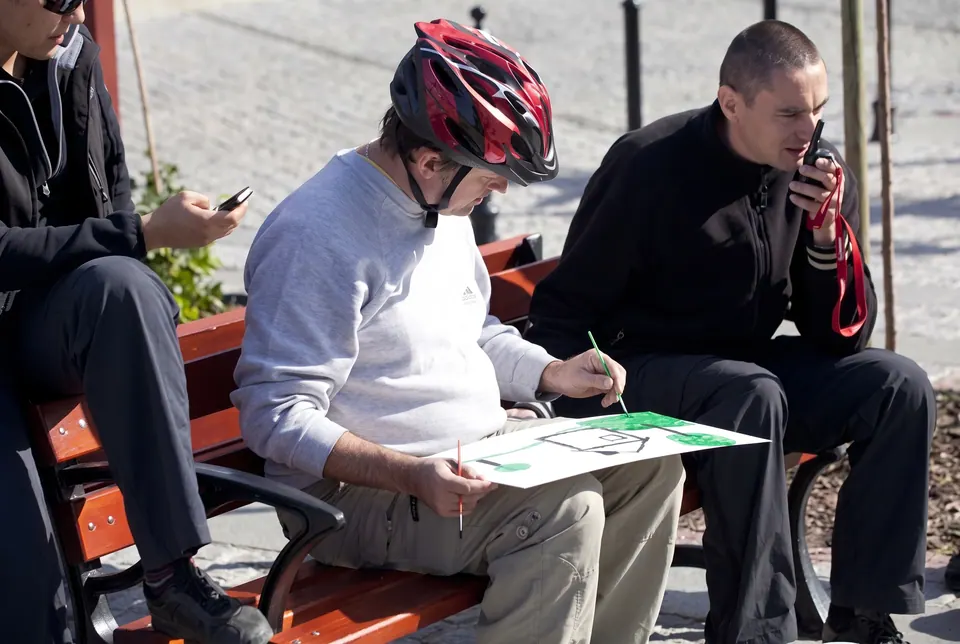 Uczestnik w kasku rowerowym rysuje na planszy, siedząc na ławce