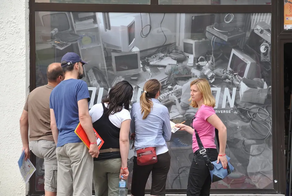 Uczestnicy gry miejskiej oglądają witrynę z plakatem przedstawiającym stare komputery